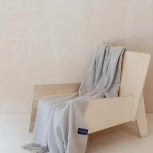 TBCo Lambswool Small Blanket in Oatmeal Melange draped over wooden chair showing soft texture and fringed edges
