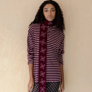 Woman wearing TBCo Merino Wool Skinny Scarf in Burgundy Flora with pale pink embroidered floral pattern against wood background