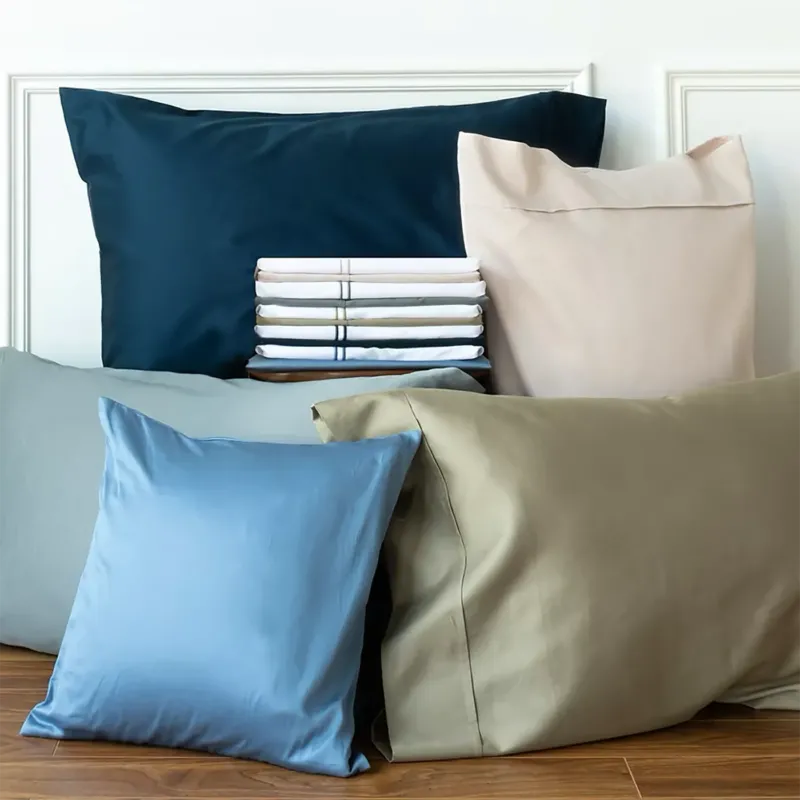 Capri Sateen pillowcases styled in navy, blush, sage, blue, and taupe with folded sheets.