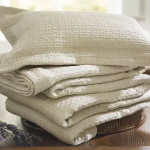 SDH Kimi ivory woven cotton pillow sham and folded bedding stacked on wood tray.